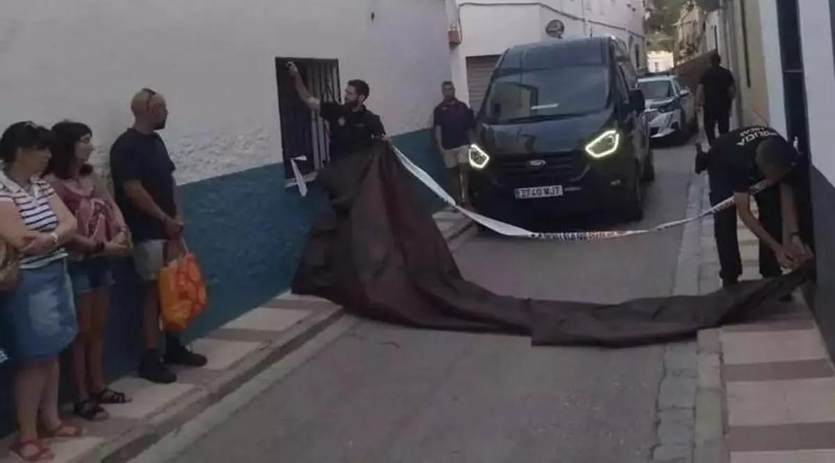 Los policías retiran el precinto para que salga el furgón de la funeraria en la calle en la que ocurrieron los hechos