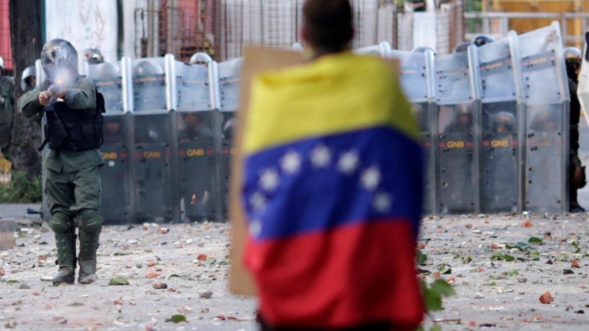 Un hombre con una bandera venezolana se enfrenta a las fuerzas de seguridad durante la Huelga General del 26 de julio.