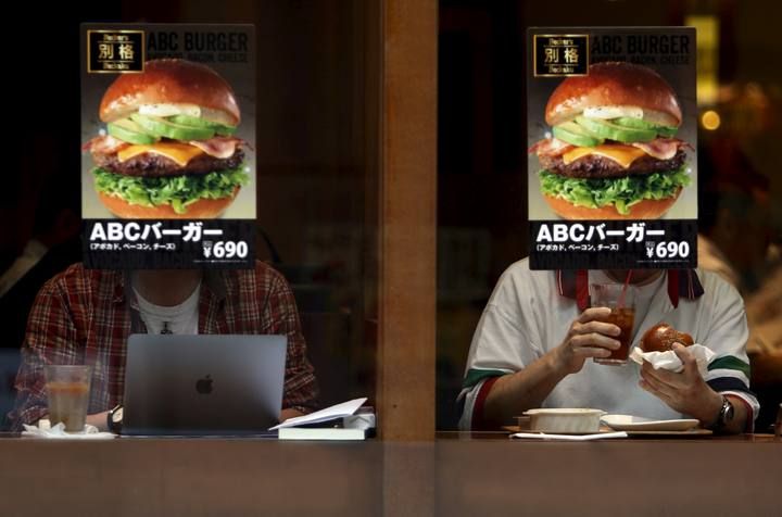 Customers sitting inside a fast food shop are seen behind its hamburger advertisement poster on a window at the Tokyo's Akihabara shopping district