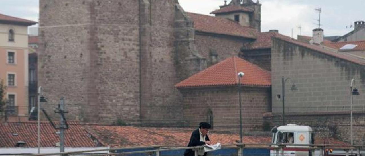 Un hombre lee el periódico acodado en la pasarela del puerto, con la iglesia de los Franciscanos al fondo.