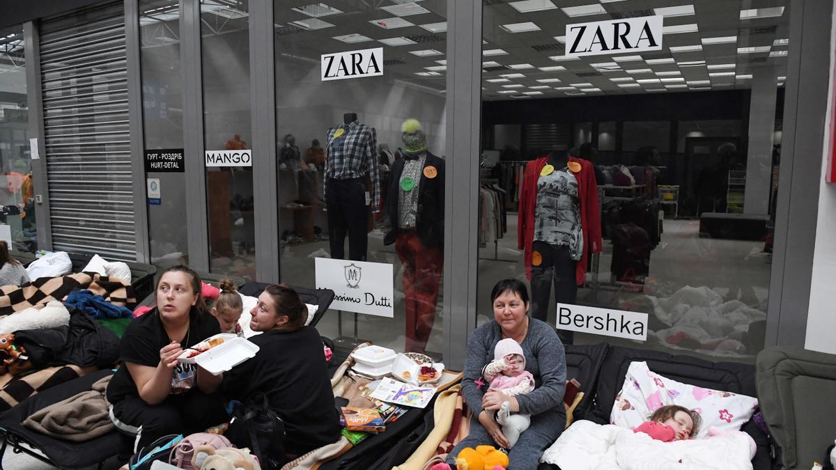 Ciudadanos ucranianos descansan en un centro de acogida de refugiados en el paso fronterizo de Korczowa, en Polonia, junto a una tienda de ropa donde se exhiben diferentes marcas, algunas de las cuales ya han anunciado su salida de Rusia, en protesta por la guerra