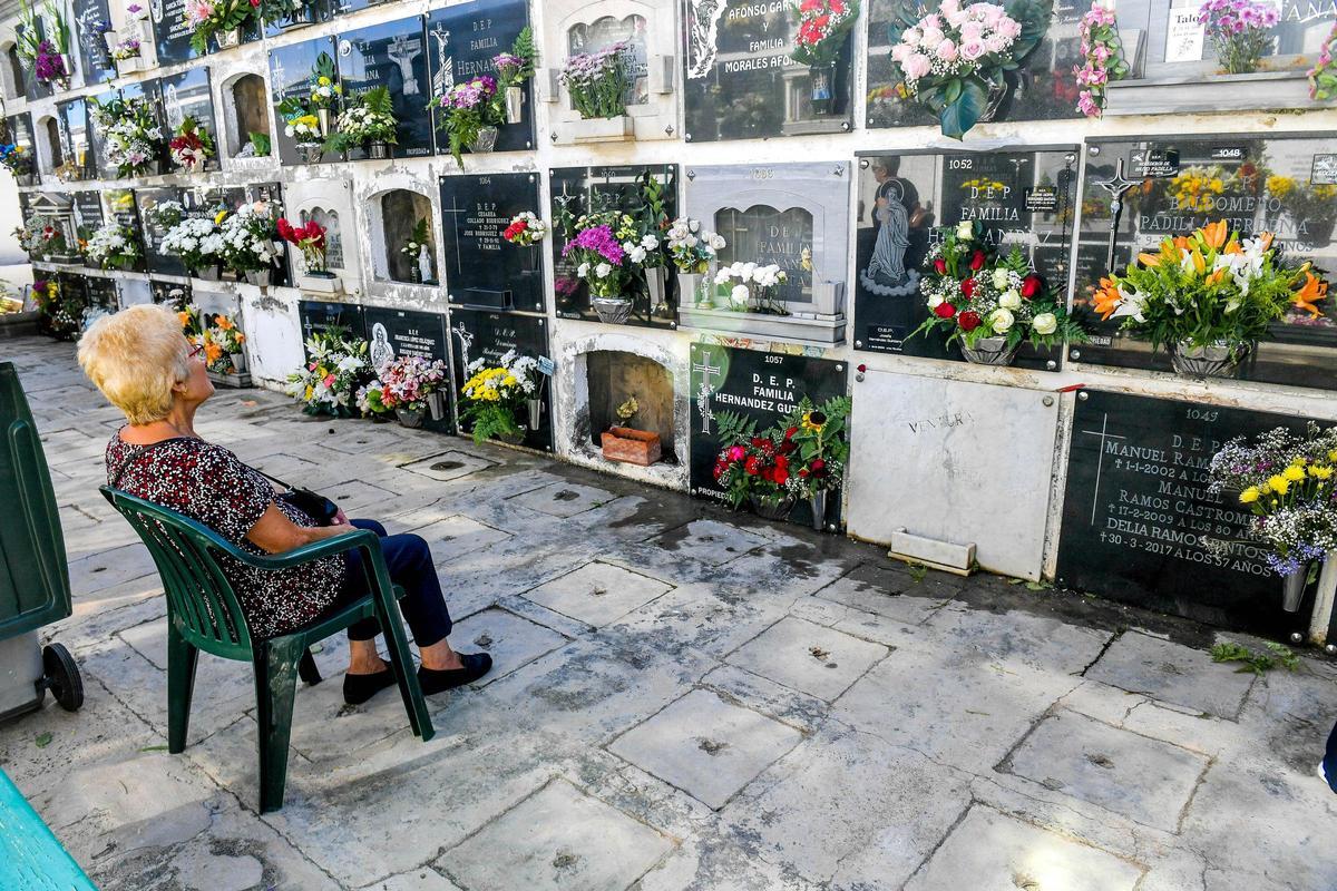 Una señora descansa delante de la tumba de sus familiares en San Juan