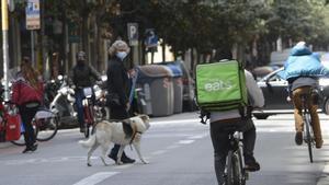 Una señora con su perro cruza por la calle de Gran de Gràcia mientras circulan varias bicicletas por el carril bus.