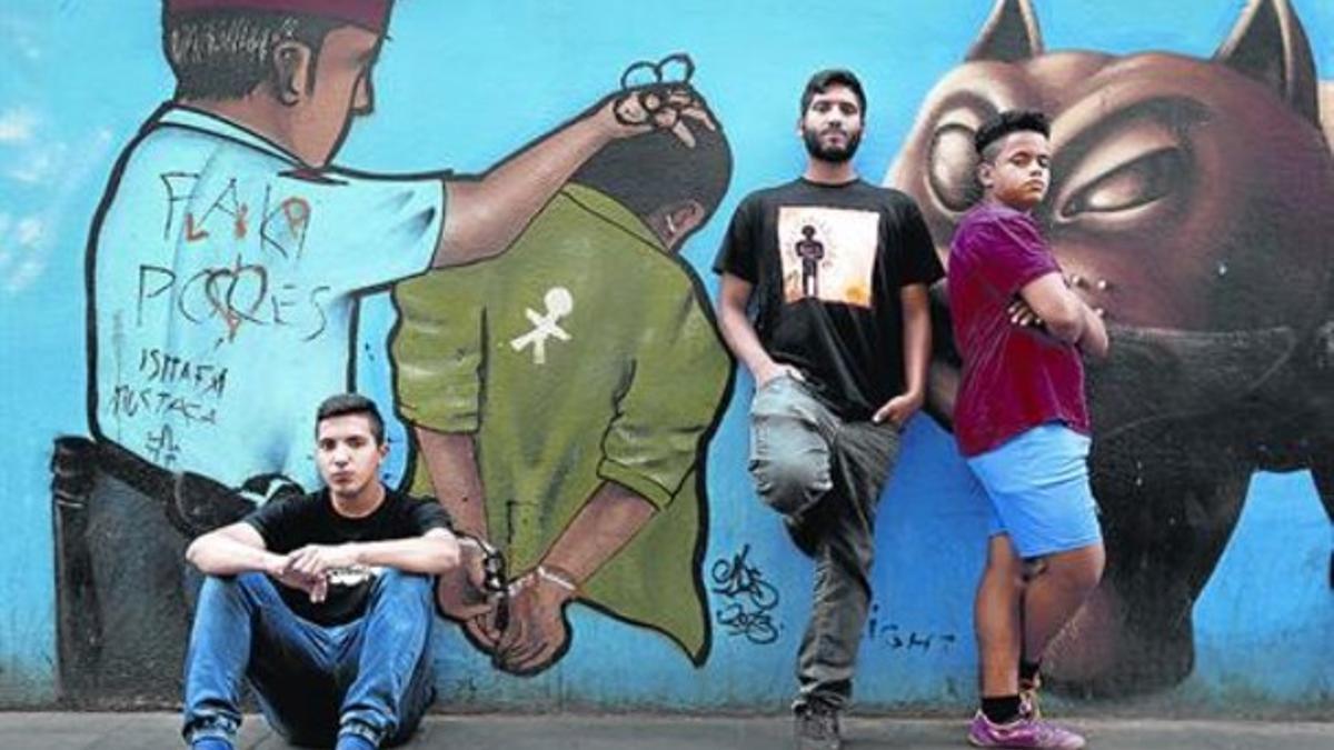 Grafito de protesta 8 Los tres miembros de La Llama posan delante de una pintada.