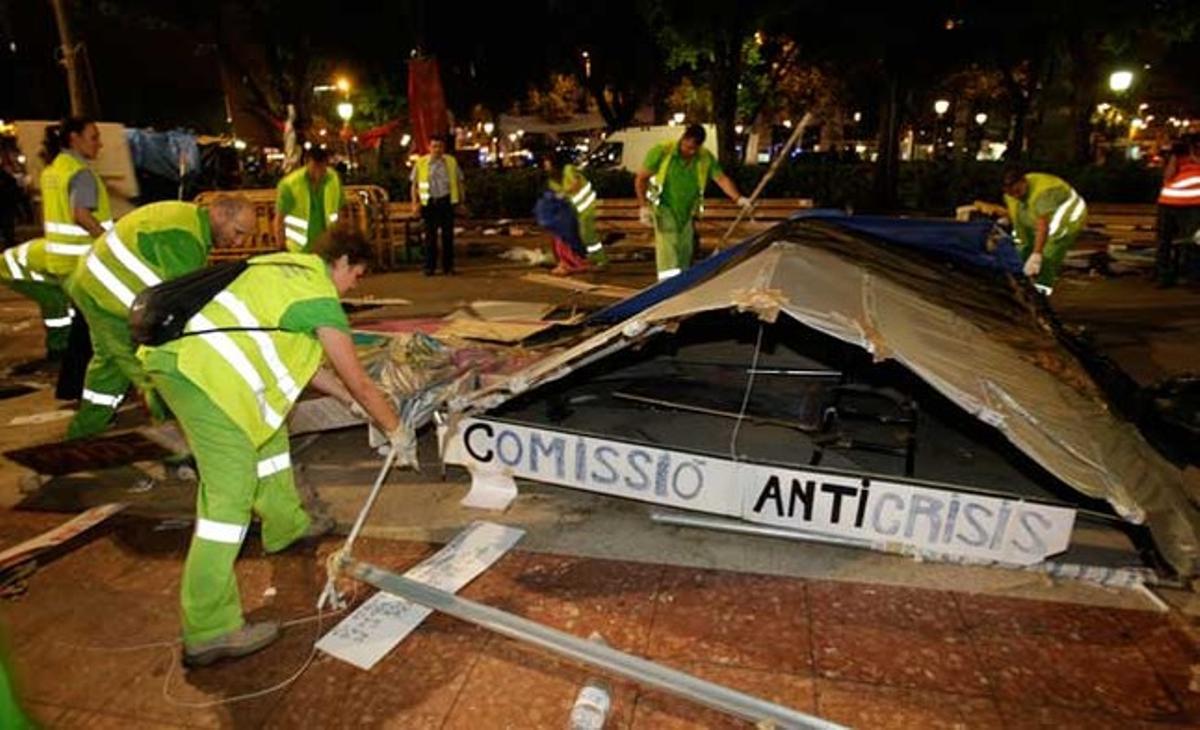 Treballadors del servei de neteja desmunten la barraca de la comissió anticrisi dels indignats.