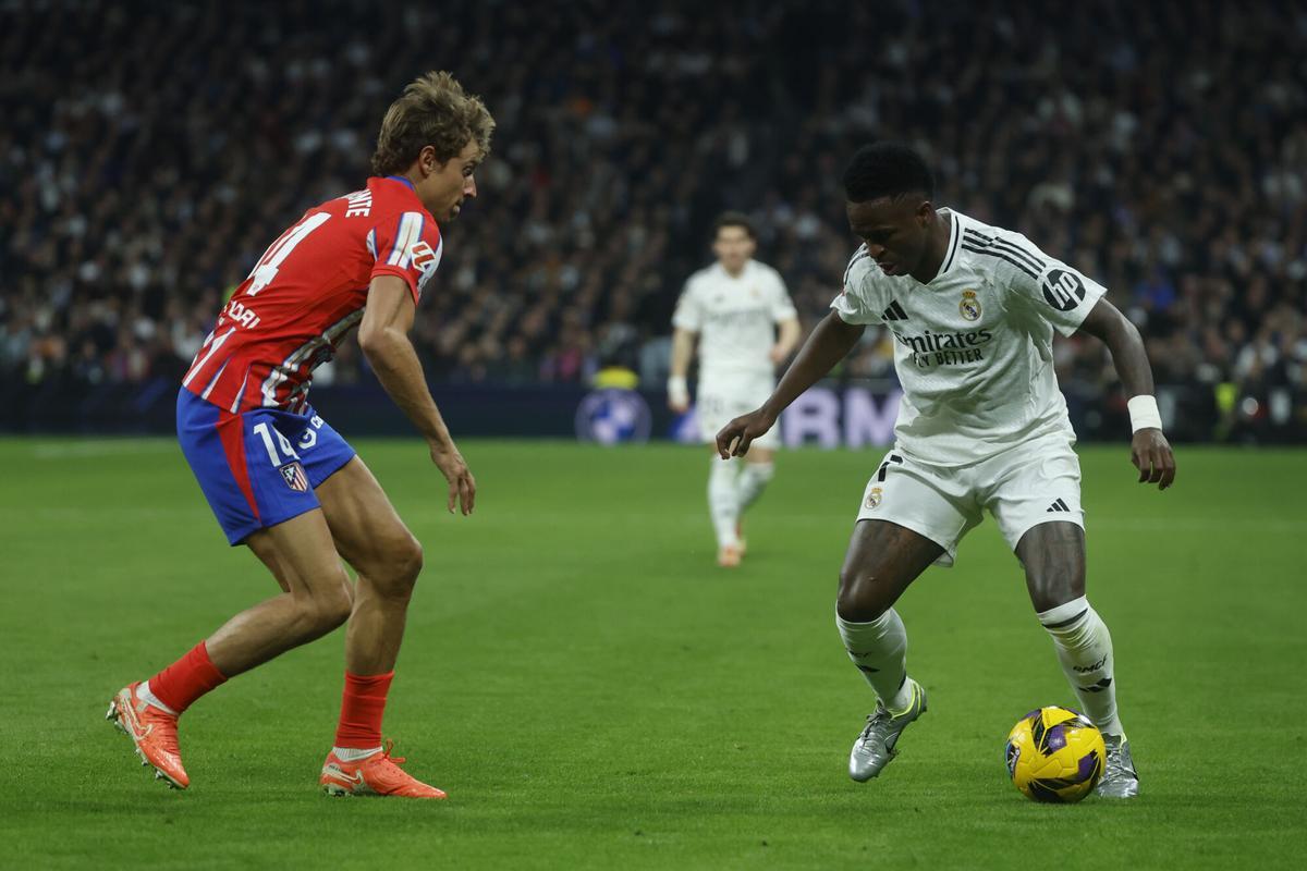 MADRID, 08/02/2025.- El delantero del Real Madrid Vinicius Jr. (d) intenta escaparse de Marcos Llorente, del Atlético de Madrid, durante el partido de la jornada 23 de LaLiga de fútbol que Real Madrid y Atlético de Madrid disputan este sábado en el estadio Santiago Bernabéu. EFE/Juanjo Martín