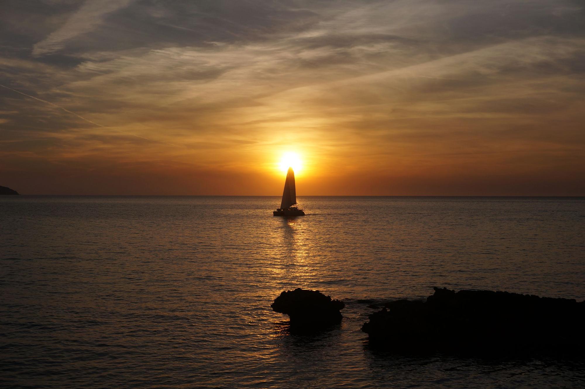 Un velero atraviesa la puesta de sol en una imagen tomada desde Cala Gració (Sant Antoni).