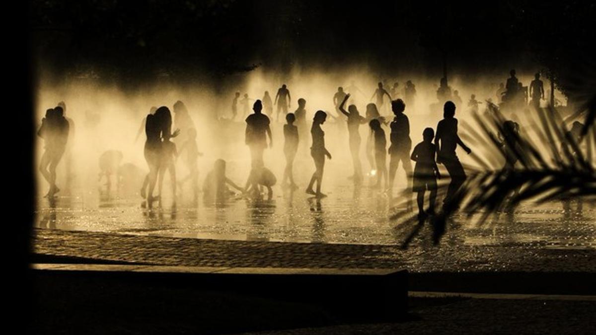 Gente refrescándose en unas fuentes al lado del río Manzanares, en Madrid.