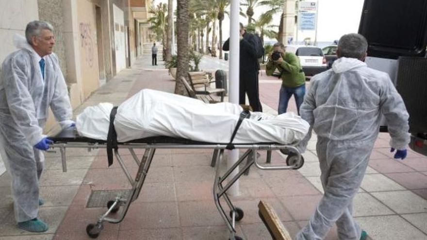 Dos trabajadores de los servicios funerarios trasladan el cadáver del fallecido.