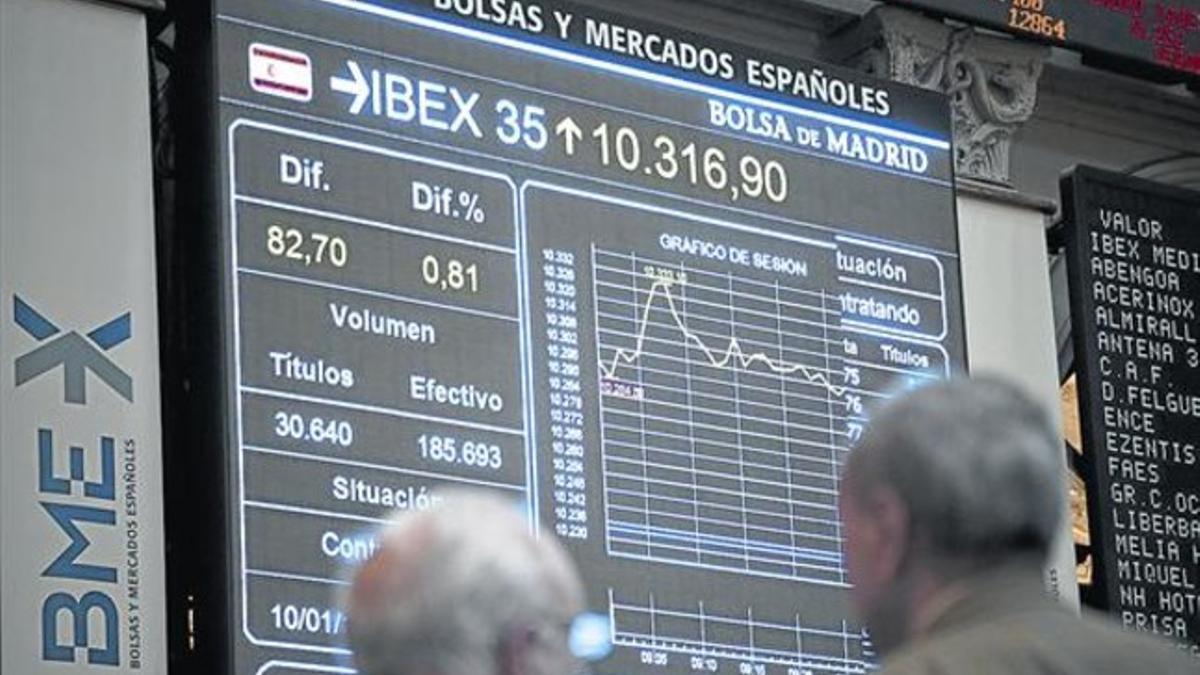 Dos inversores observan una pantalla con la evolución del Ibex 35 en la Bolsa de Madrid.