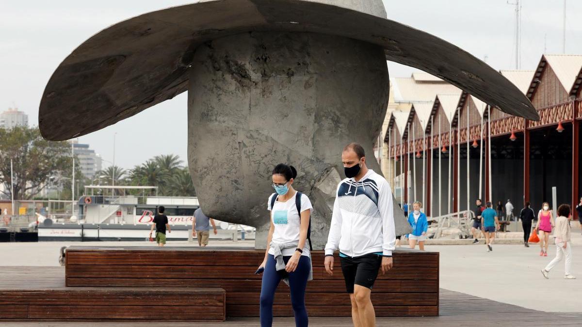 Dos personas pasean con mascarilla por la dársena de València.