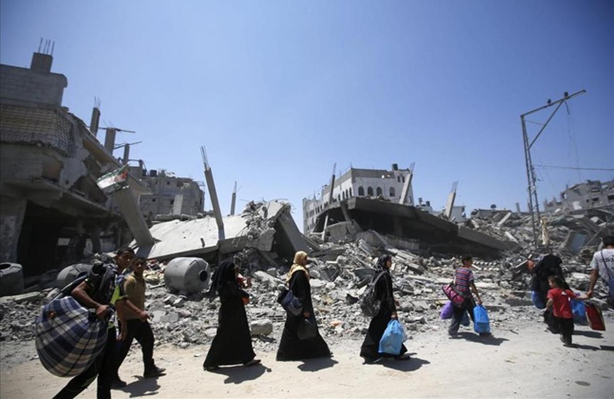 Varios palestinos pasan junto a un edificio derruido mientras transportan sus pertenencias en el barrio de Al-Shejaeiya, en el este de la ciudad de Gaza.