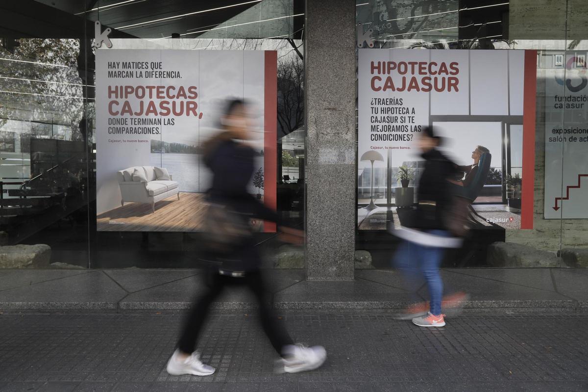 Viandantes caminan frente a la publicidad de una entidad financiera.