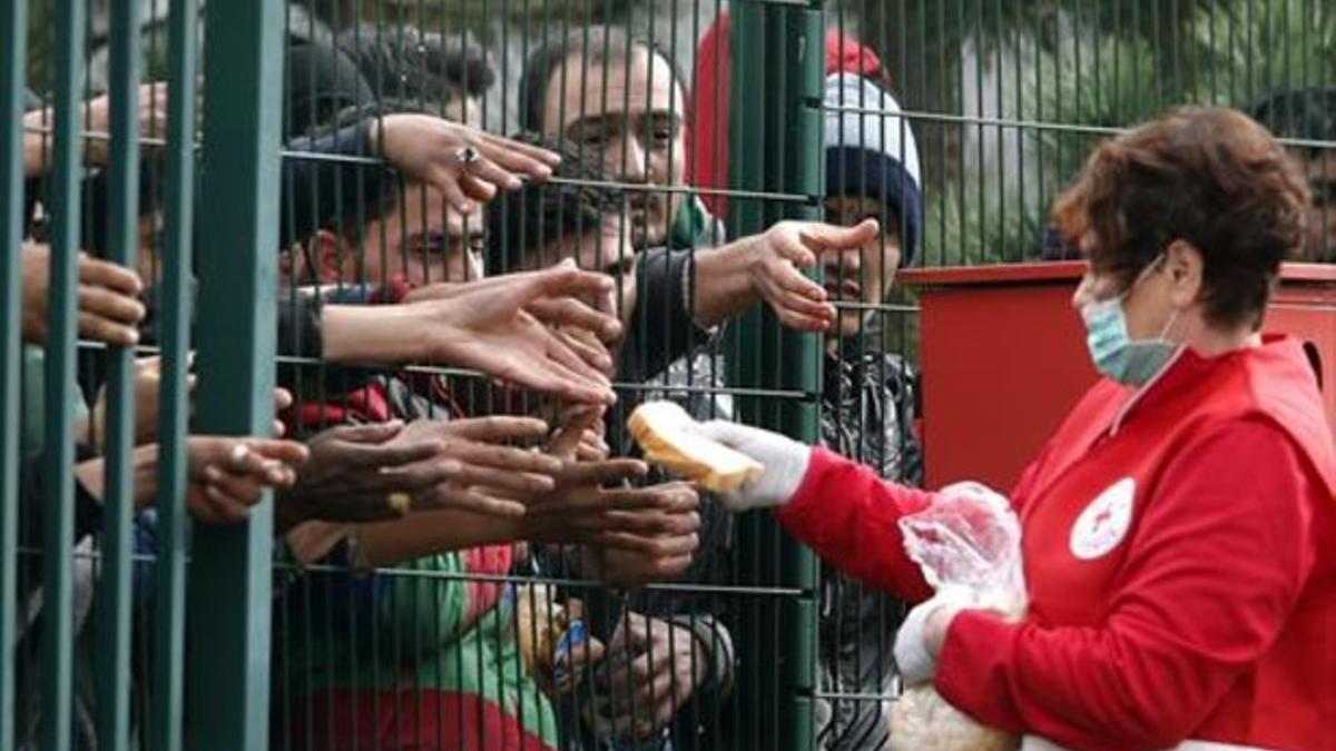 Una trabajadora de la Cruz Roja ofrece pan a los refugiados tras una valla en el campo de acogida de Brezice, este miércoles.