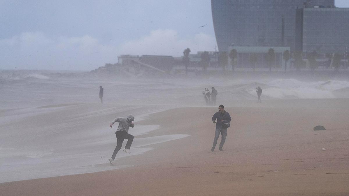 Varias personas desafían el mal tiempo y el oleaje en la playa de la Barceloneta