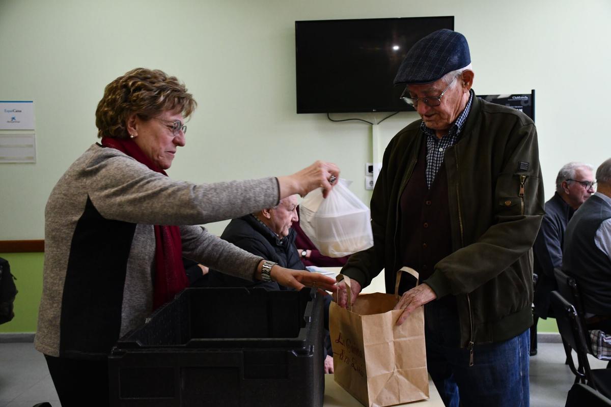 Ramon Solans, de 87 años, a la derecha, recoge su comida preparada en la cocina del colegio Sol Ixent de Corbins (Segrià), de manos de una voluntaria de la asociación de jubilados.