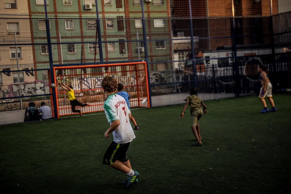 Un grupo de niños juegan a fútbol en la pista del parque de La Granada de l'Hospitalet de Llobregat, en el marco de el proyecto 'Espais Oberts per un Estiu Enriquit'.