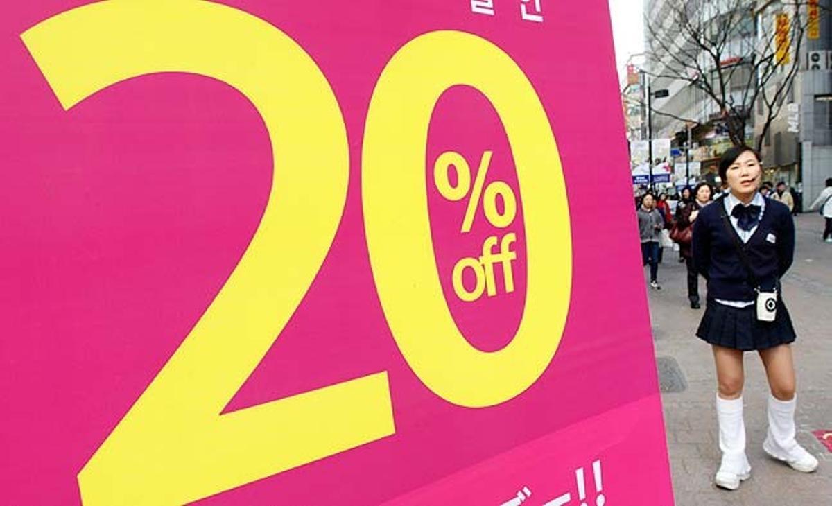 Una venedora d’una botiga de cosmètics espera al carrer per intentar atraure clients, al districte comercial de Myeongdong, a Seül (Corea del Sud).