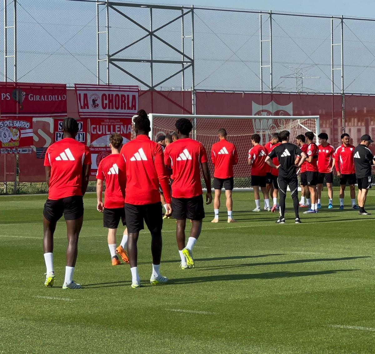 Los jugadores del Sevilla miran las banderas de las peñas colocadas en una de las lonas del campo de entrenamiento de la CD José Ramón Cisneros Palacios