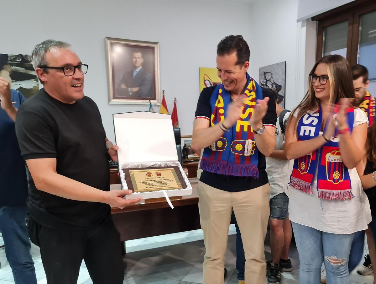 Pacual Pérez mostrando la placa de agradecimiento del Ayuntamiento de Elda en presencia del alcalde Rubén Alfaro y de la concejala de Deportes.