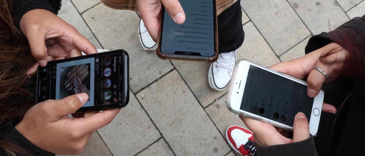 Tres jóvenes hacen uso de sus teléfonos móviles