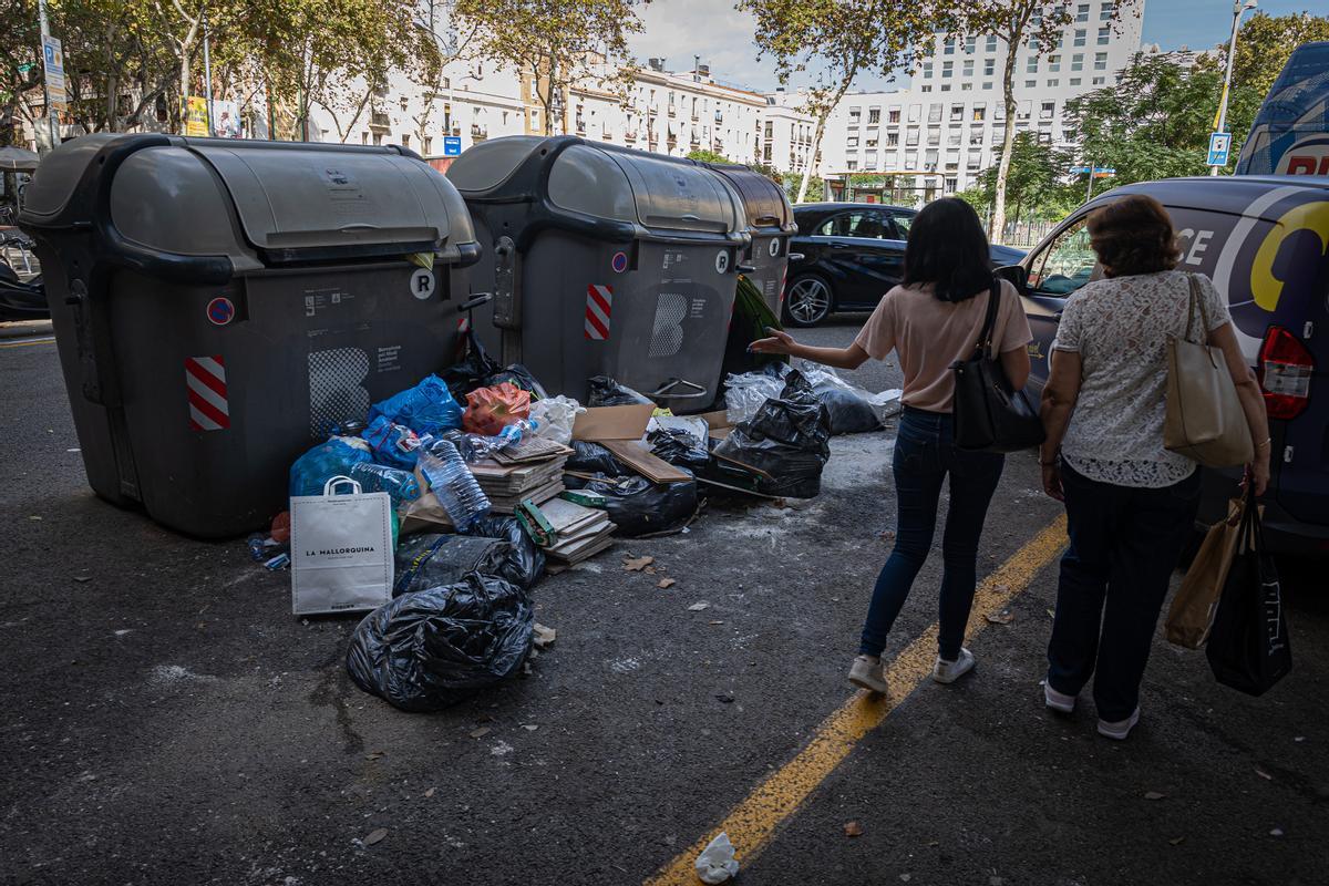 Dos mujeres comentan la sociedad acumulada junto a unos contenedores en el Eixample.