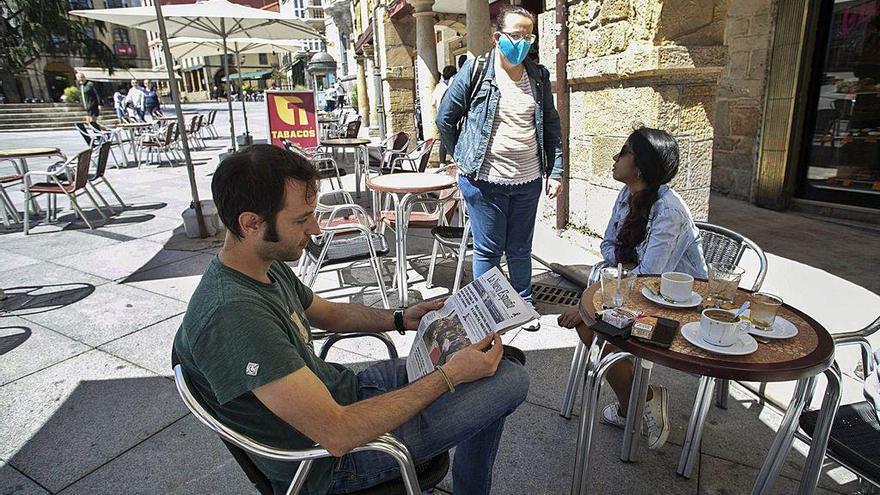 Un joven lee LA NUEVA ESPAÑA en la terraza de un bar de Avilés.