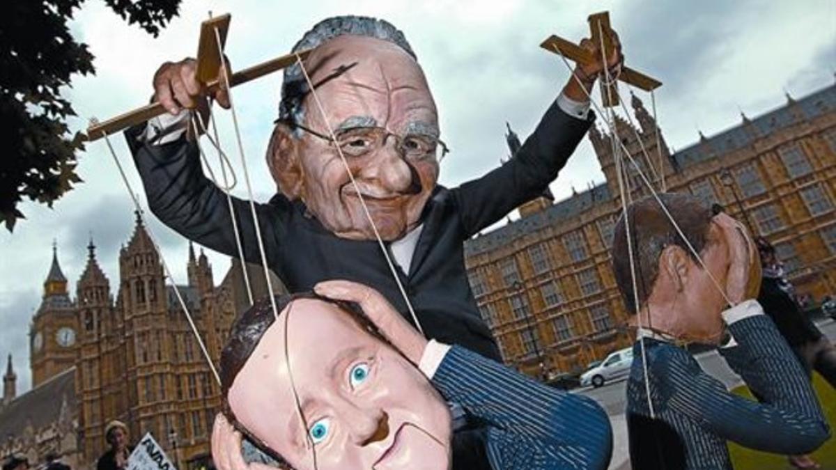 Un manifestante con una máscara de Murdoch, el dueño del imperio mediático del que aún forma parte 'News of the World', mueve las marionetas del primer ministro Cameron y del titular de Cultura y Medios, Hunt, frente al Parlamento británico, el viern