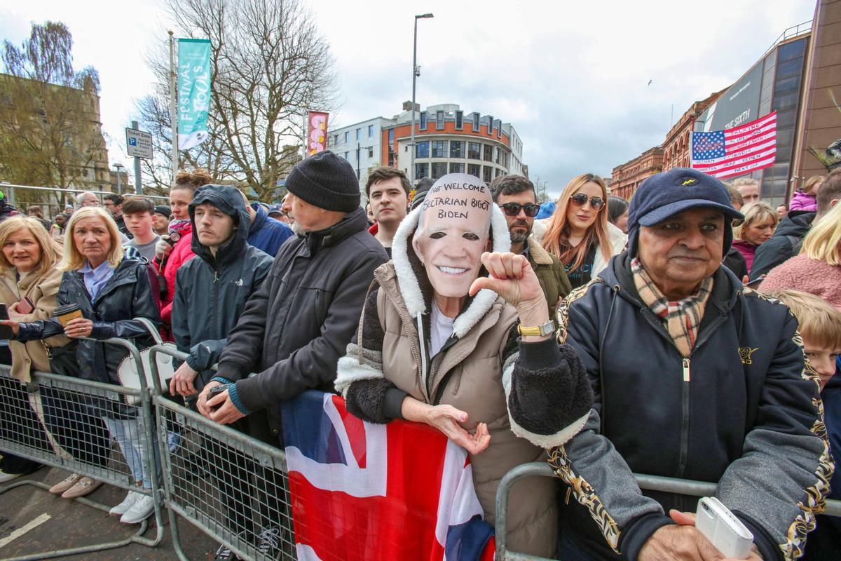 Un manifestante con una máscara que representa al presidente de los Estados Unidos, Joe Biden, se encuentra frente a la Universidad de Ulster, mientras el presidente de los Estados Unidos pronuncia un discurso en el interior.