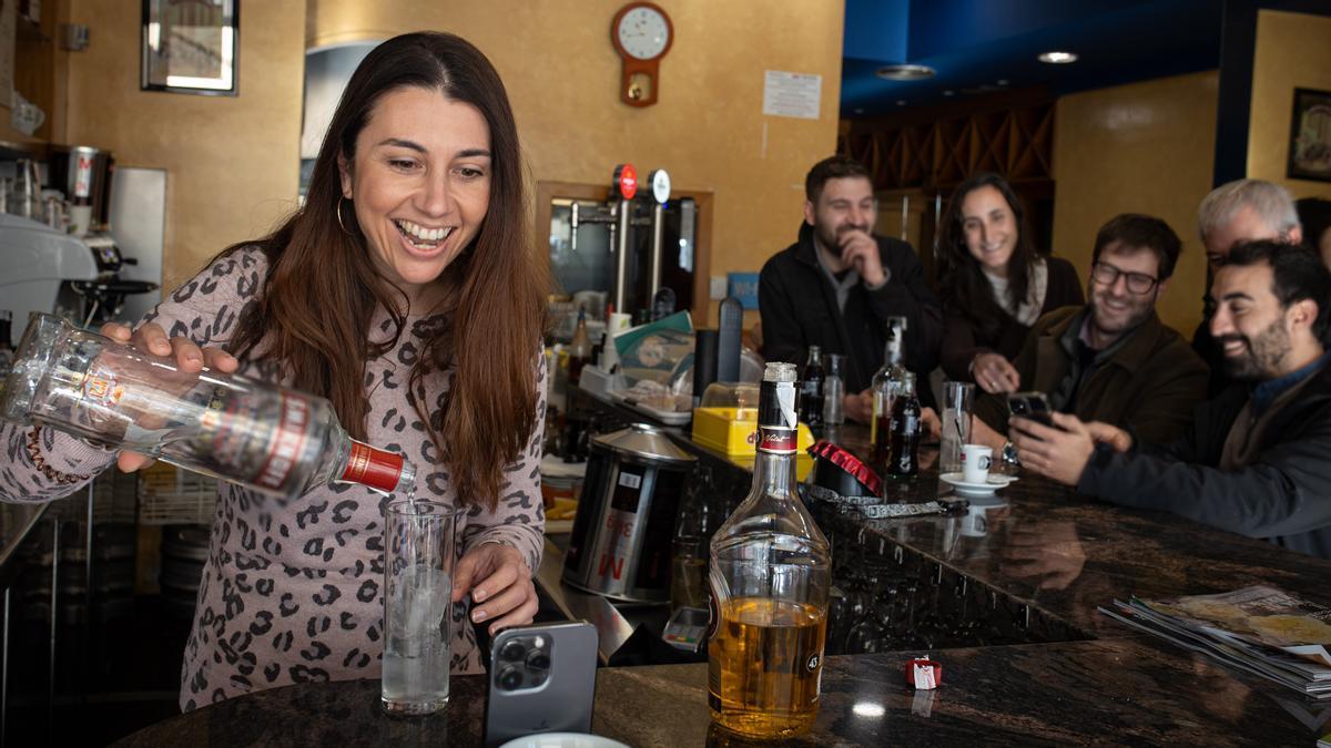 Esther carga una copa frente al móvil delante de unos clientes.