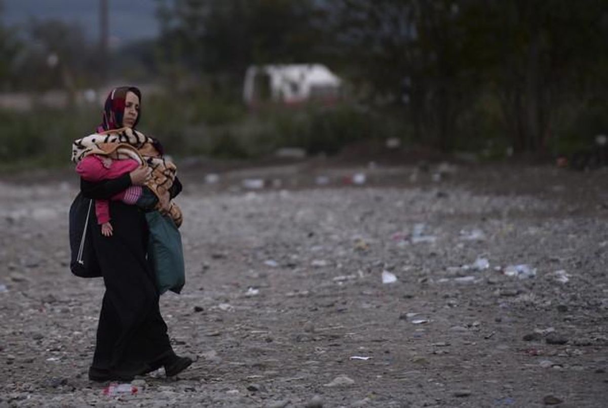 Una mujer lleva a su hijo, mientras se dirige al campo de registro después de cruzar la frontera entre Grecia y Macedonia cerca de la ciudad de Gevgelija.