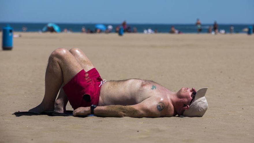 Un hombre descansa al sol en la arena de la Malvarosa.