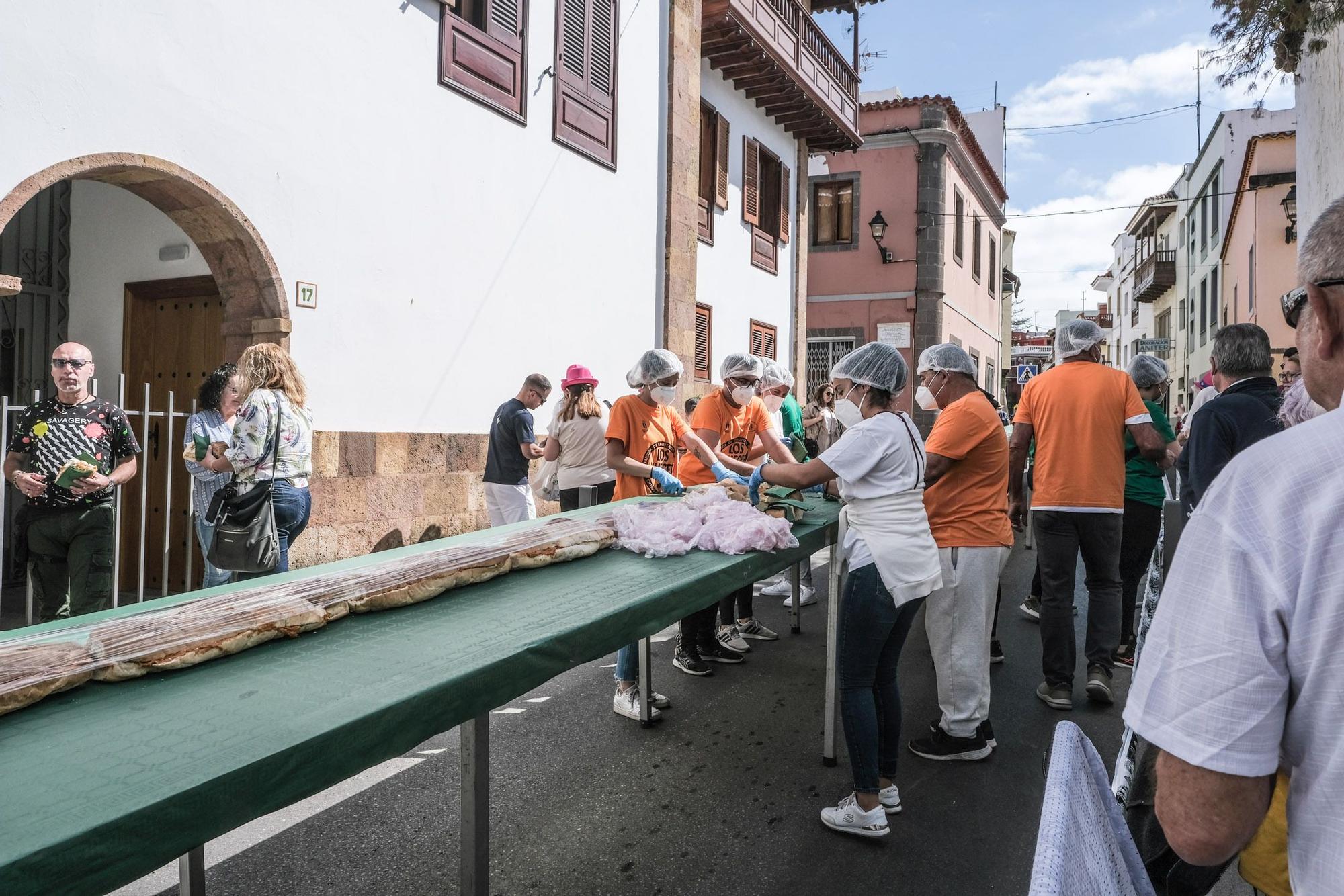 Los voluntarios reparten las raciones de bocadillo de chorizo gigante en la Calle Nueva de Teror.