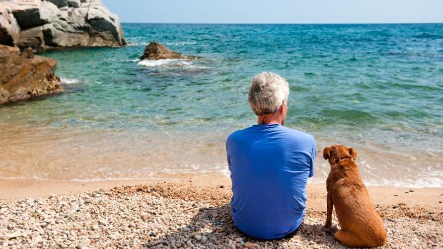 Un hombre reposa con su perro frente al mar en una playa de acceso permitido a animales.