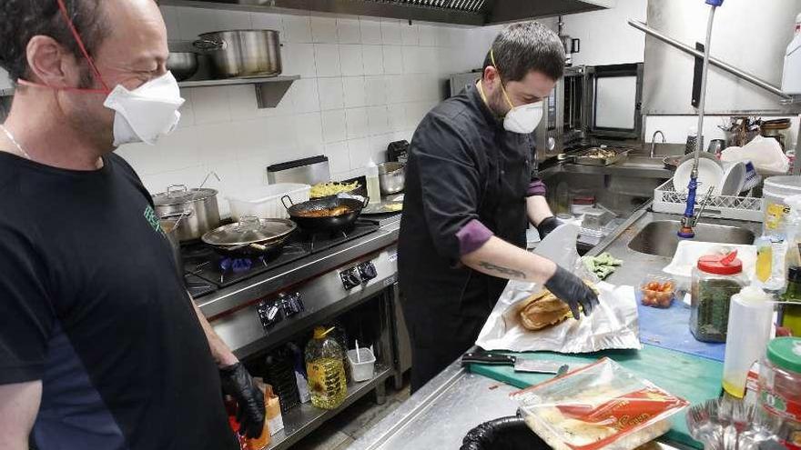 El camarero Carlos García y el cocinero Manuel Andújar preparan con guantes y mascarillas un menú en el hotel gijonés