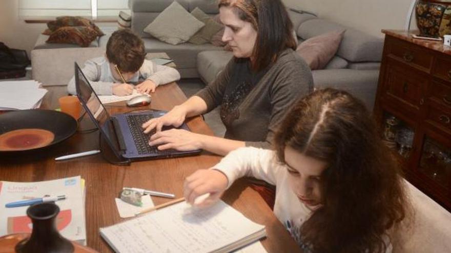 Una mujer teletrabaja mientras sus hijos hacen los deberes.