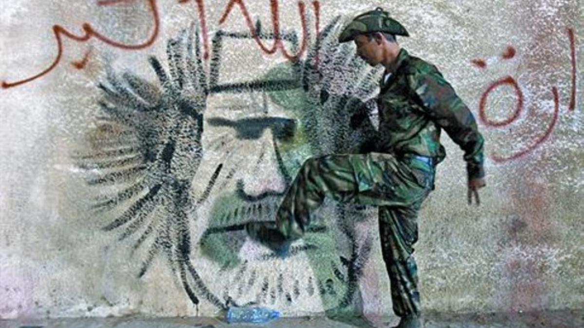 Un combatiente rebelde patea un grafito con la cara de Gadafi bajo la inscripción 'Dios es grande', ayer.