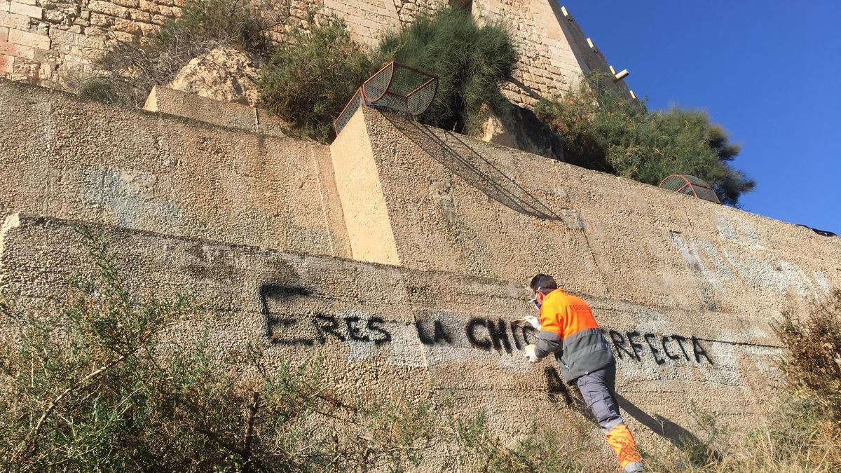 Un operario municipal limpiando esta mañana la pintada realizada en el muro del castillo de Petrer.