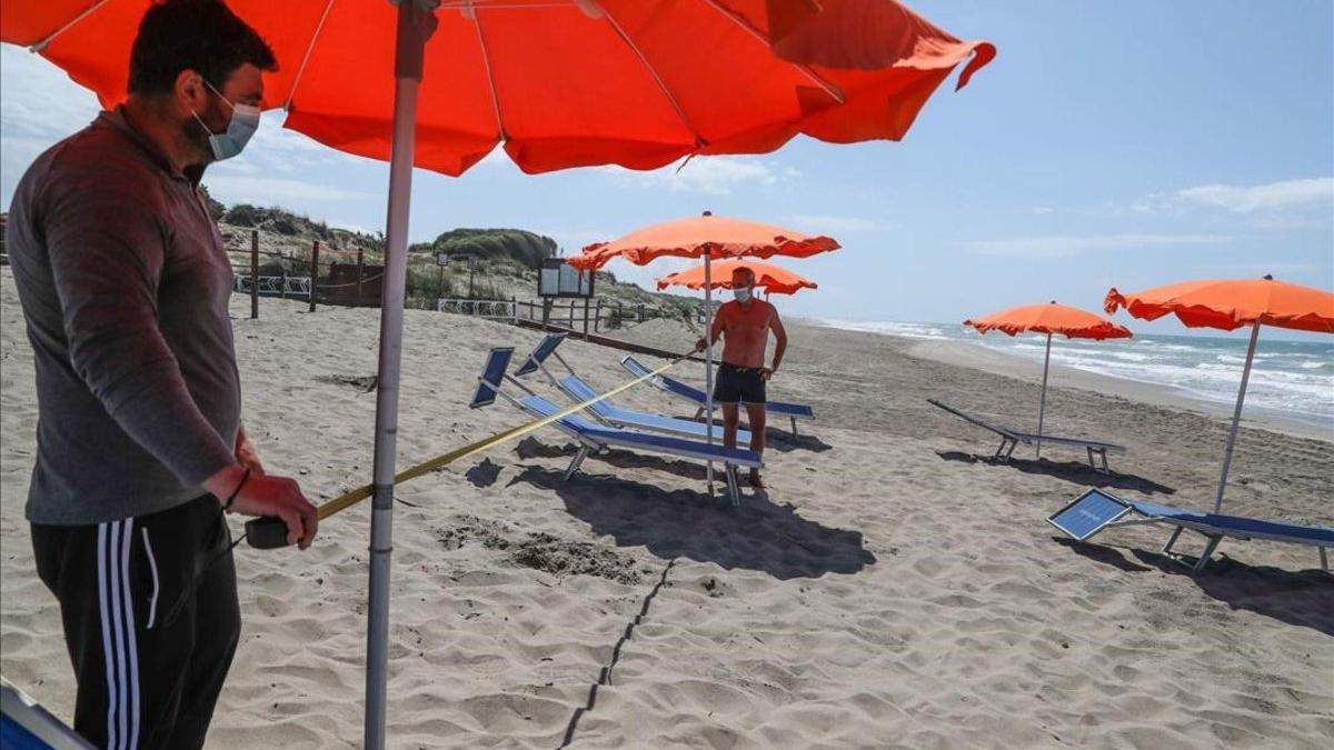 Dos trabajadores con mascarillas en la playa italiana de Copocotta, cerca de Roma.