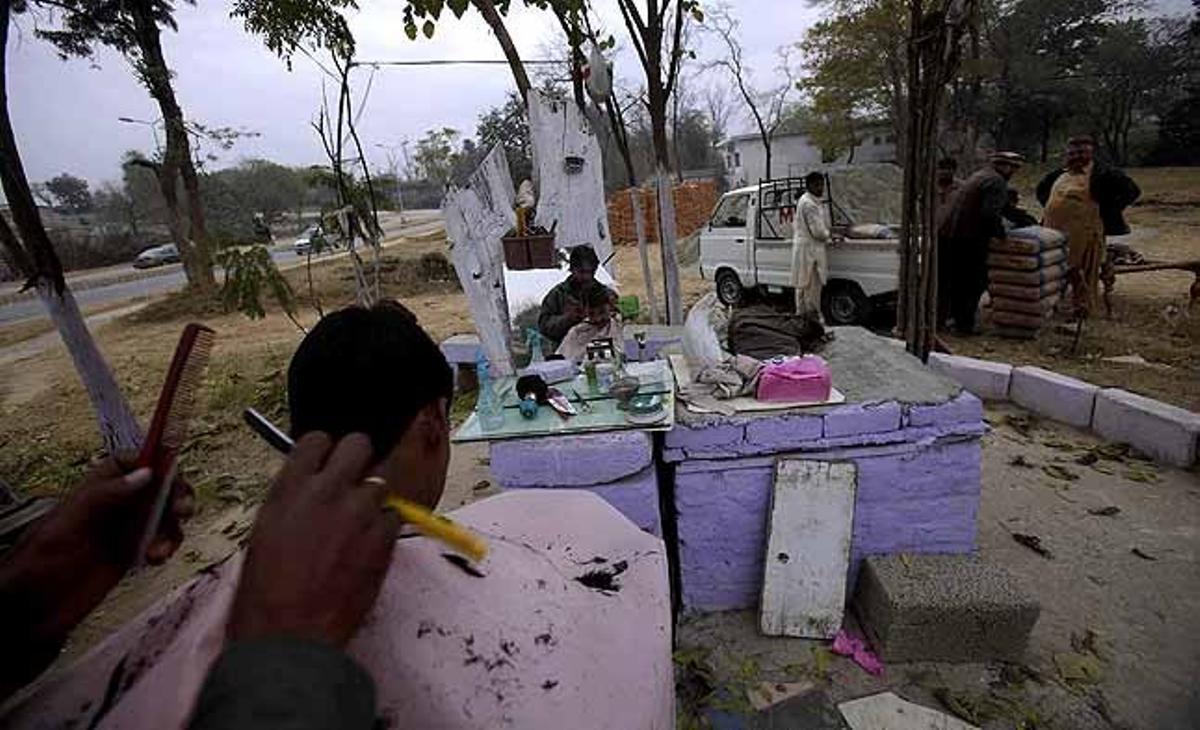 Un pakistanès es talla els cabells en una perruqueria que està instal·lada al carrer a Islamabad (Pakistan).