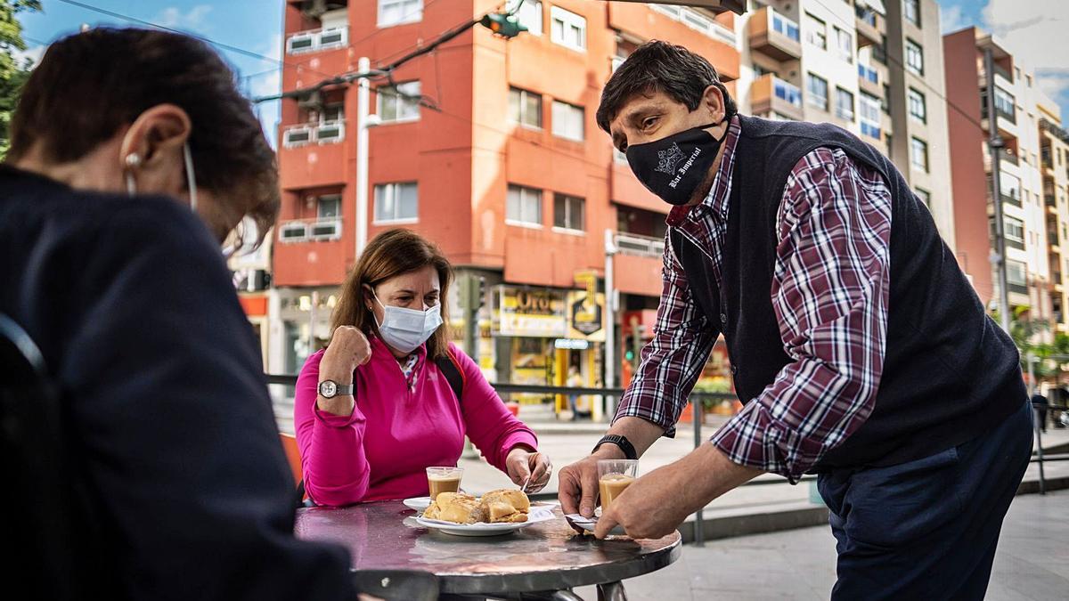 Un camarero sirve a unos clientes en la mesa de una terraza.