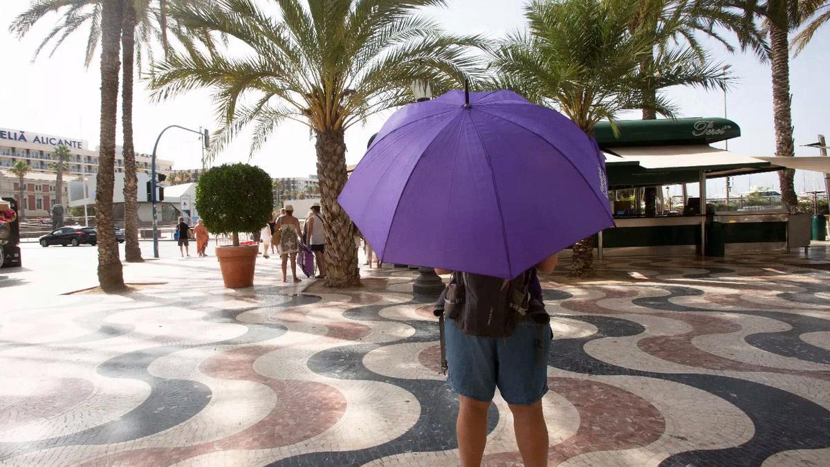 Un hombre se resguarda del sol con un paraguas en la Explanada de Alicante