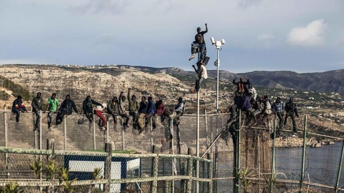 Inmigrantes africanos sentados encima de la valla de la frontera que separa Marruecos del norte de África en Melilla