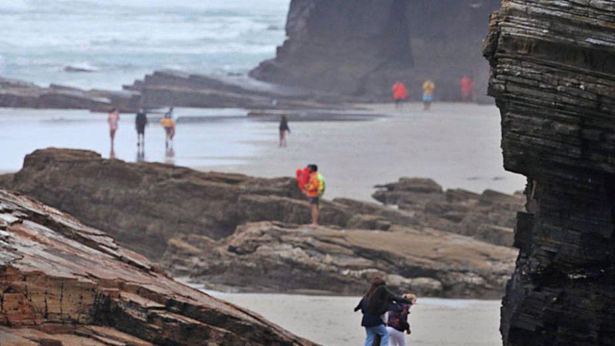 Turistas y vigilantes con mascarillas en la playa de As Catedrais.