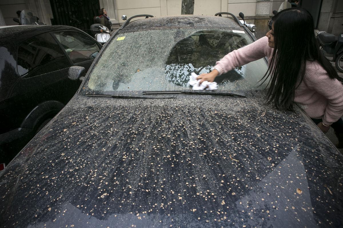 Mujer limpiando un coche manchado con barro por las 'lluvias de sangre' en Barcelona.