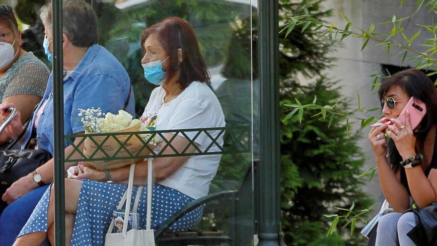 Una mujer fuma junto a un aparada de autobús.