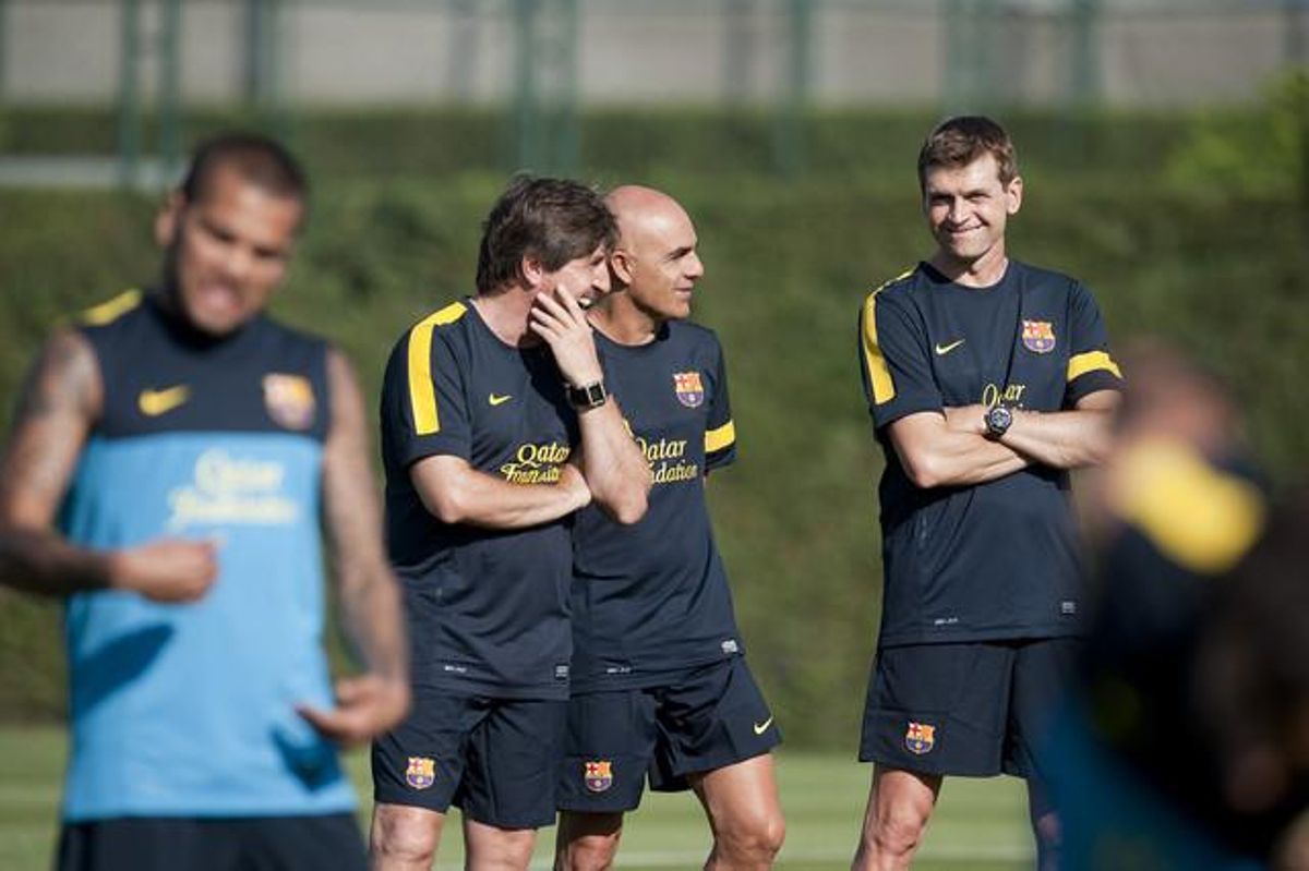 En un primer pla, Tito i Roura supervisen l’entrenament dels jugadors i Alves, en segon pla, fa els exercicis d’escalfament.