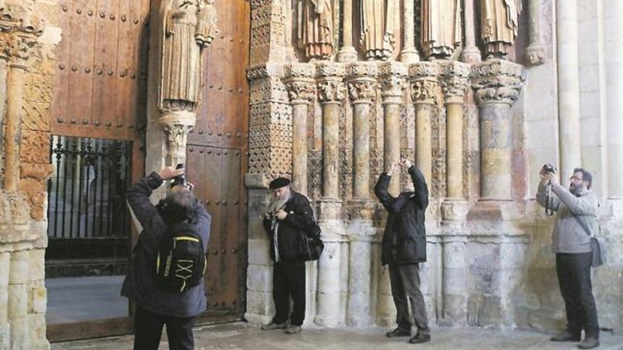 Varias personas fotografían los detalles del Pórtico de la Gloria en la Colegiata.