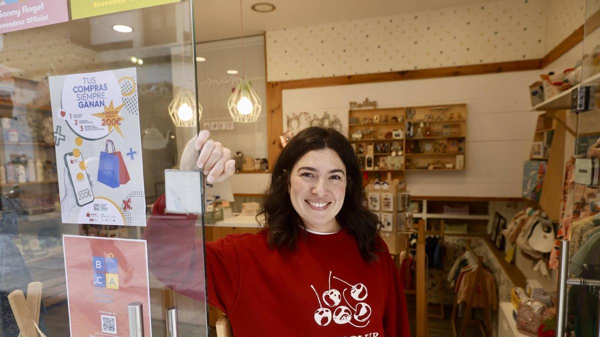 Una comerciante participante en la última edición de "Gijón compra y vuelve", junto al cartel del programa.