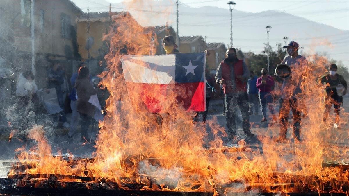 Un manifestante sostiene una bandera de Chile frente a una barricada ardiendo durante una protesta en Santiago de Chile, este lunes.